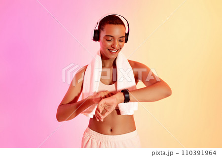 A happy woman with a shaved head wearing headphones checks her fitness tracker after a workout 110391964
