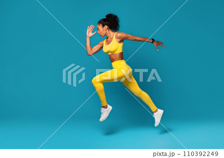 Athletic black woman leaping during dynamic workout on blue backdrop Athletic black woman leaping during dynamic workout on blue backdrop 110392249