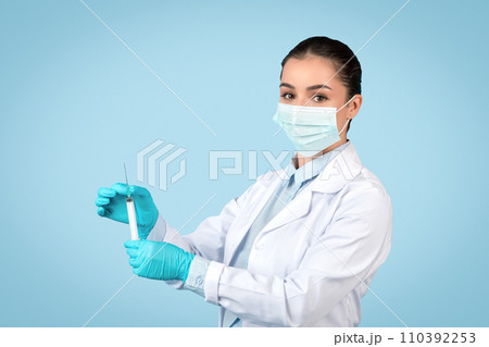 Focused woman doctor with syringe, protective gear on Focused woman doctor with syringe, protective gear on 110392253