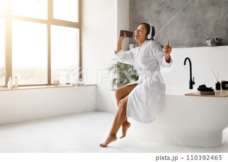 Black woman in white bathrobe singing into her phone as microphone, 110392465