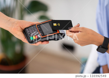 Hands of lady hold black contactless credit card over card reader to complete payment 110392549