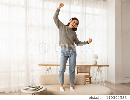 Cheerful young Caucasian lady in wireless headphones listening to music 110392588