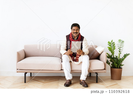 Relaxed mature eastern man chilling at home, using tablet Relaxed mature eastern man chilling at home, using tablet 110392618
