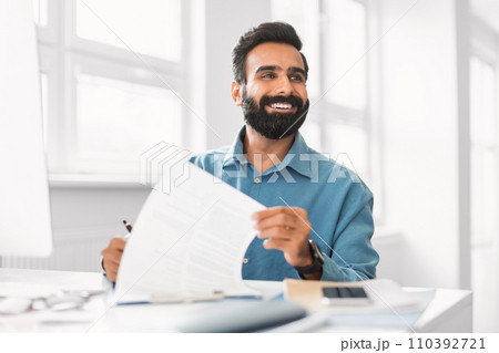 Smiling indian executive reviewing a document at his desk 110392721