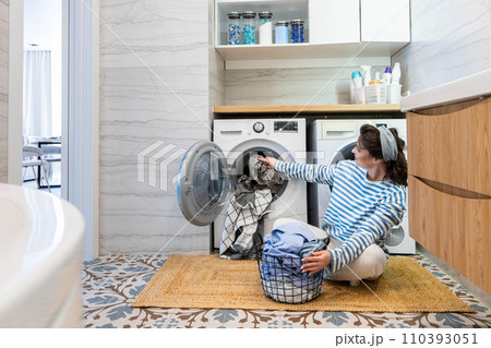 Modern housewife putting dirty linen textile and clothes to washing machine at domestic laundry Modern housewife putting dirty linen textile and clothes to washing machine at domestic laundry 110393051