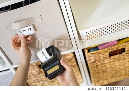 Woman mother applying paper sticker with name title on basket container clean out of childish toys 110393112
