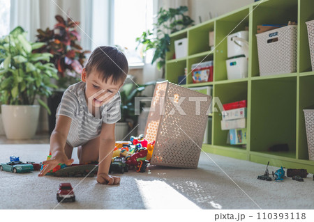 A cheerful European boy plays with cars on the carpet in his room. A cheerful European boy plays with cars on the carpet in his room. 110393118