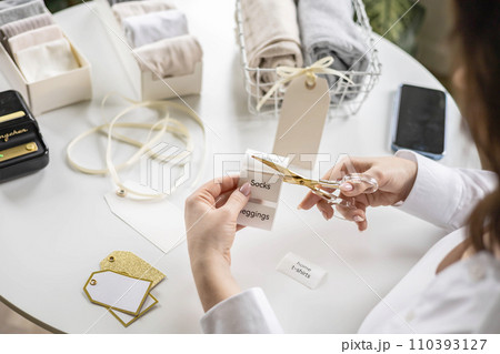 Woman hands cutting sticker tag scissors comfortable storage organizing linen textile in container Woman hands cutting sticker tag scissors comfortable storage organizing linen textile in container 110393127