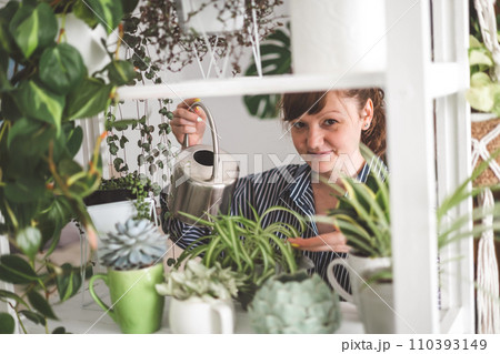 A young woman enjoys caring for flowers. Watering indoor plants and admiring them. 110393149