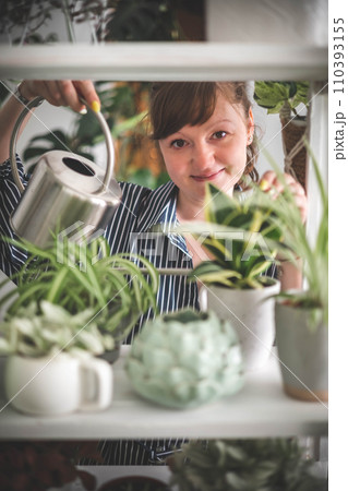 A young woman enjoys caring for flowers. Watering indoor plants and admiring them. 110393155