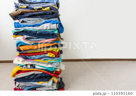 A very tall stack of folded colored clothes for charity, washing, ironing and sorting. 110393160