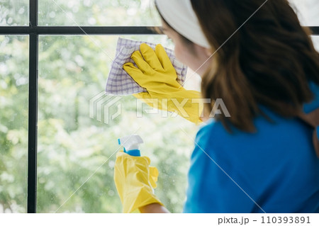 A young woman wearing gloves joyfully sprays and wipes office windows. Her cleaning routine emphasizes purity care and hygiene ensuring transparent sparkling windows. A young woman wearing gloves joyfully sprays and wipes office windows. Her cleaning routine emphasizes purity care and hygiene ensuring transparent sparkling windows. 110393891