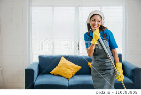 Happy Asian housewife sings her favorite song using mop as microphone during cleanup making household chores fun. Dancing and cleaning in living room cheerful maid enjoying her routine. Happy Asian housewife sings her favorite song using mop as microphone during cleanup making household chores fun. Dancing and cleaning in living room cheerful maid enjoying her routine. 110393908