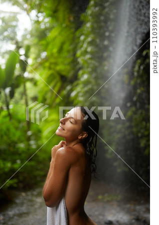 A young slender nude woman covers herself with a towel near an incredibly beautiful waterfall in a cliff on the popular island of Bali. A young slender nude woman covers herself with a towel near an incredibly beautiful waterfall in a cliff on the popular island of Bali. 110393992