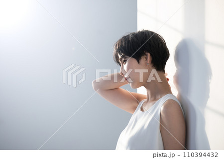 窓際の白い壁に寄りかかり日差しを浴びる黒髪ショートの若い女性の横顔上半身 110394432