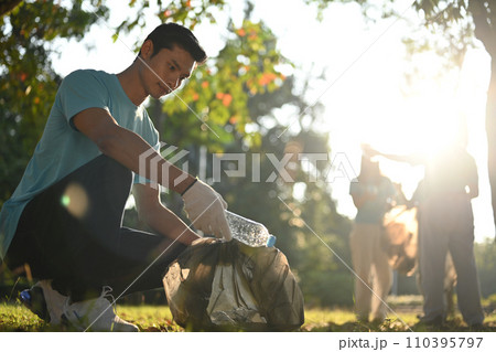 Young man volunteer picking bottles into plastic black bag for cleaning up nature. Environmental and ecology concept Young man volunteer picking bottles into plastic black bag for cleaning up nature. Environmental and ecology concept 110395797