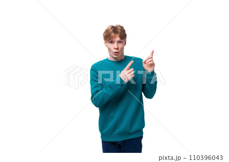 handsome red-haired young man in a blue sweater points his hands up 110396043