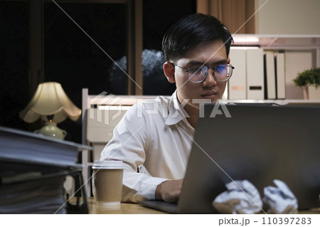 Young businessman working overtime on a desk at night.. 110397283