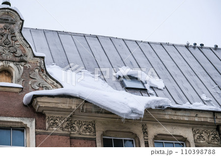 A lump of snow and ice on the edge of the roof of the house. Thaw, chalking snow danger in the city. A lump of snow and ice on the edge of the roof of the house. Thaw, chalking snow danger in the city. 110398788