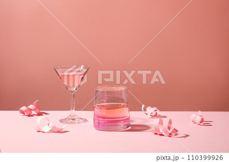 A cup and a cocktail glass decorated against pink background with paper fireworks. Concept of creative Christmas and New Year composition for template 110399926