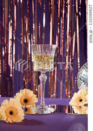 A glass of champagne on a Silver foil tinsel strips background with highlights for christmas and new year concept. Some flowers displayed with a mirror 110399927