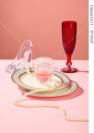 A stack of ceramic dish with a cup of pink liquid placed on top. Red wine glass and a glass high heel displayed. Celebration background concept with pink tone A stack of ceramic dish with a cup of pink liquid placed on top. Red wine glass and a glass high heel displayed. Celebration background concept with pink tone 110399961