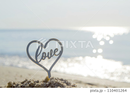 Plastic stick in shape of heart and word Love in sand on beach seashore on sunny summer day close-up. Figures in shape of heart word Love on background of sea waves. Love relationship romance concept Plastic stick in shape of heart and word Love in sand on beach seashore on sunny summer day close-up. Figures in shape of heart word Love on background of sea waves. Love relationship romance concept 110401264