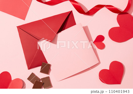 A pink card, a red envelope, red paper hearts, ribbons and chocolates are displayed on a pastel pink background. Valentine's Day theme for advertising. A pink card, a red envelope, red paper hearts, ribbons and chocolates are displayed on a pastel pink background. Valentine's Day theme for advertising. 110401943
