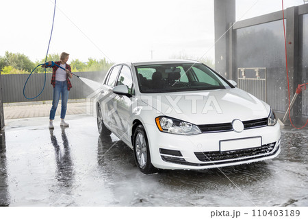 Woman in red shirt cleaning the car with a hose Woman in red shirt cleaning the car with a hose 110403189