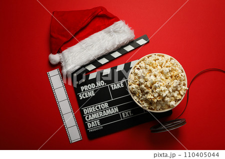 Reel, film, popcorn in paper cup, clapperboard and Santa's hat on red background, top view Reel, film, popcorn in paper cup, clapperboard and Santa's hat on red background, top view 110405044