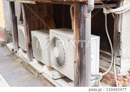 古い家屋の屋外に並んだエアコンの室外機 古い家屋の屋外に並んだエアコンの室外機 110405477