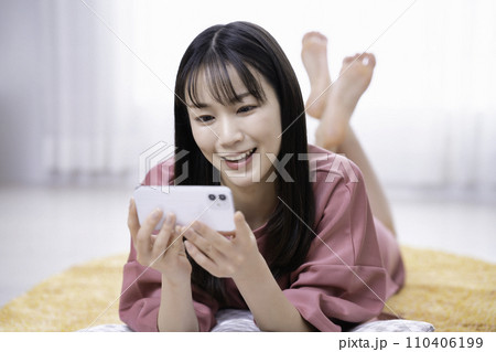 カーペットに寝転んでスマホ動画を観る女性 110406199