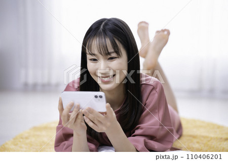 カーペットに寝転んでスマホ動画を観る女性 110406201