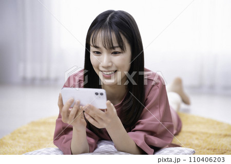 カーペットに寝転んでスマホ動画を観る女性 110406203