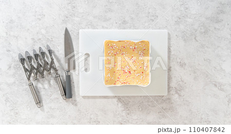 Flat lay. Removing candy cane fudge from a square cheesecake pan lined with parchment. 110407842