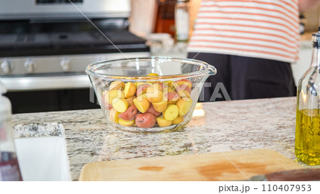 In a sleek, modern kitchen, a young man attentively prepares dinner. His current task involves carefully seasoning small rainbow potatoes in a glass bowl, promising a flavorful meal ahead. In a sleek, modern kitchen, a young man attentively prepares dinner. His current task involves carefully seasoning small rainbow potatoes in a glass bowl, promising a flavorful meal ahead. 110407953