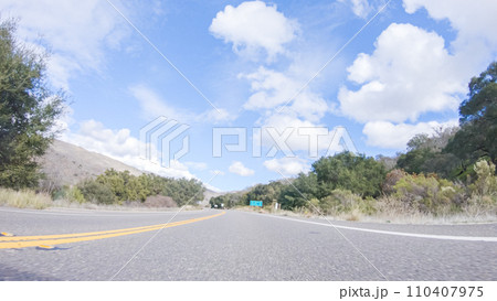 Vehicle is cruising along the Cuyama Highway under the bright sun. The surrounding landscape is illuminated by the radiant sunshine, creating a picturesque and inviting scene as the car travels 110407975