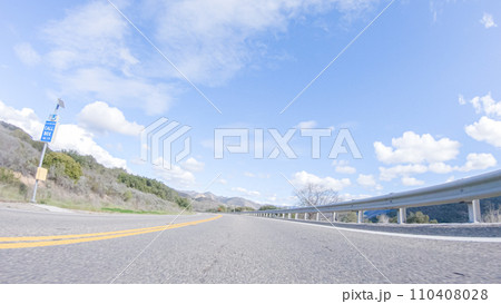 Vehicle is cruising along the Cuyama Highway under the bright sun. The surrounding landscape is illuminated by the radiant sunshine, creating a picturesque and inviting scene as the car travels 110408028