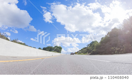 On a clear winter day, a car smoothly travels along Highway 101 near Santa Maria, California, under a brilliant blue sky, surrounded by a blend of greenery and golden hues. 110408040