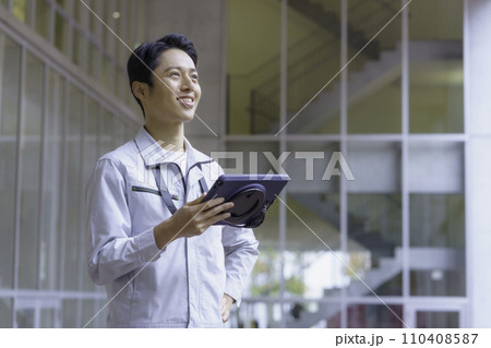 作業服を着てタブレットを見る若い男性　撮影協力:有明教育芸術短期大学 110408587