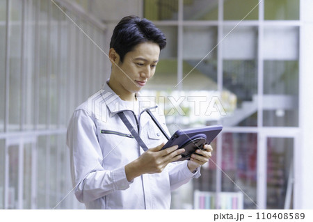作業服を着てタブレットを見る若い男性　撮影協力:有明教育芸術短期大学 110408589