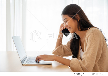 Young asian woman talking mobile smartphone while working on computer laptop 110409350
