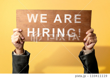 The businessman's hand shows the wooden board with We Are Hiring letters The businessman's hand shows the wooden board with We Are Hiring letters 110411119