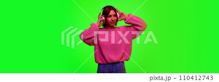 Banner. Young beautiful girl posing puts headphones on head against green studio background with negative space to insert text. 110412743
