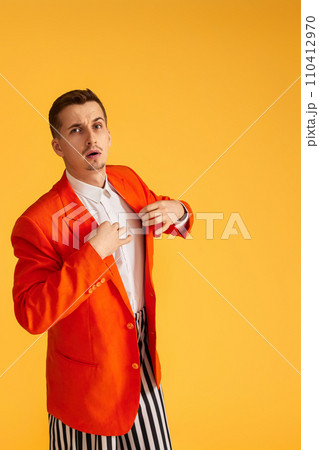 extravagant young man in orange jacket and striped pants on yellow background. extravagant young man in orange jacket and striped pants on yellow background. 110412970