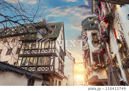 Scenic sunset view Christmas Strasbourg city street decorated Xmas toy ribbon tree beautiful warm dusk sky. Traditional Alsatian half-timbered fachwerk houses on old medieval european town center 110413749