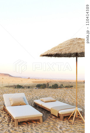 Desert oasis with elegant outdoor loungers under a thatched umbrella, offering a peaceful retreat with a view 110414389