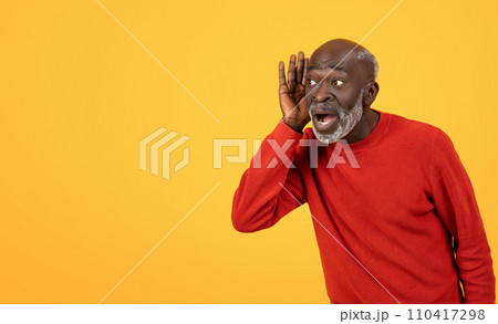 Shocked senior Black man in red sweater, hand to ear, listening intently Shocked senior Black man in red sweater, hand to ear, listening intently 110417298
