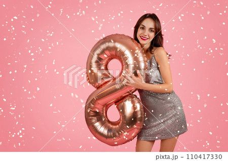 Radiant woman in a shimmering dress holding a rose gold number 8 balloon Radiant woman in a shimmering dress holding a rose gold number 8 balloon 110417330