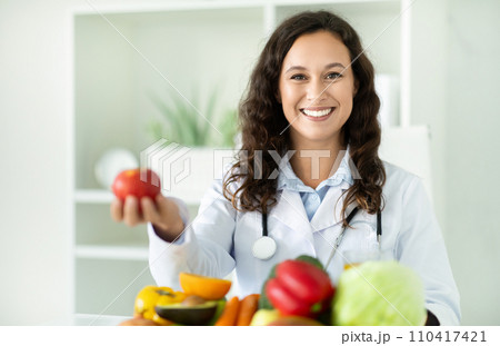Young european woman dietitian holding apple, sitting at desk at clinic Young european woman dietitian holding apple, sitting at desk at clinic 110417421
